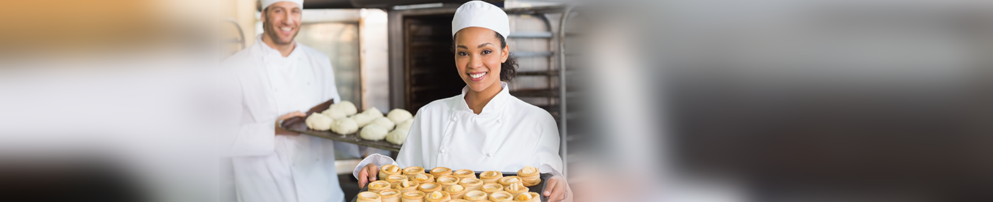 Two baking and pastry chefs holding up trays of pastries and dough. 