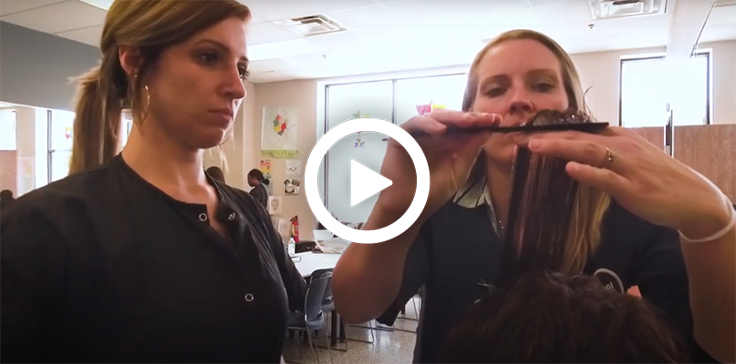 Video play button, with a cosmetology instructor teaching a student.