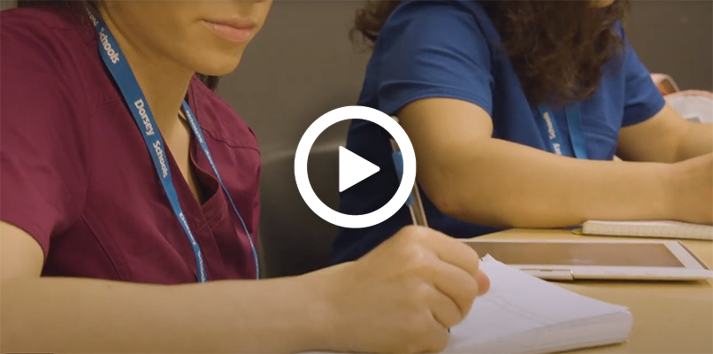 Video play button with students taking down notes in medical billing and coding classes.